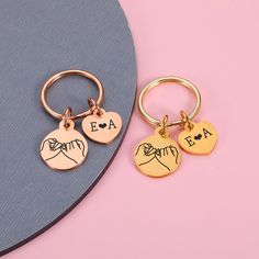 two personalized keychains on a pink and blue surface with the word fa written in gold