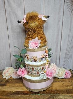 a three tiered cake decorated with flowers and an animal on top is sitting on a wooden table