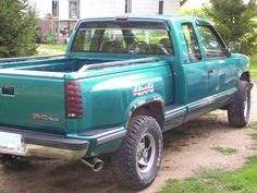 a green pick up truck parked on the side of a road in front of a house