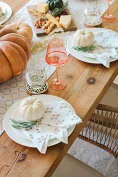 a wooden table topped with white plates and pumpkins