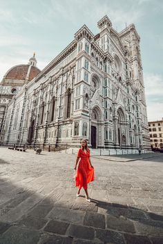 a woman standing in front of a large building with a red dress on it's side