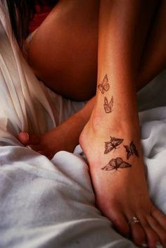 a woman laying in bed with her foot on the pillow and butterfly tattoos on her arm