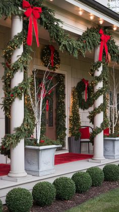 the front porch decorated for christmas with wreaths and evergreen garland on it's pillars