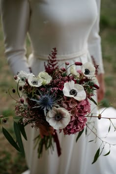 a woman holding a bouquet of flowers in her hands and wearing a white dress with long sleeves