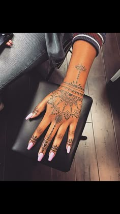 a woman's hand with henna tattoos on her left arm and wrist, sitting in front of a chair