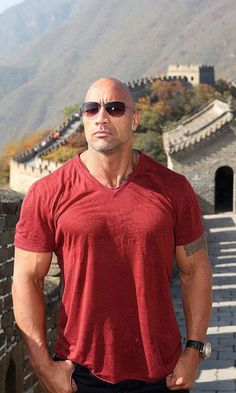 a man standing in front of a stone wall with mountains in the backgroud