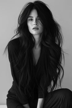 a black and white photo of a woman with long hair sitting on the floor in front of a wall