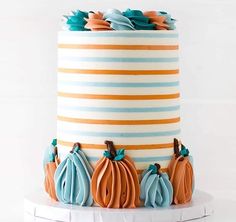 a multi - colored striped cake decorated with pumpkins and leaves on a white stand