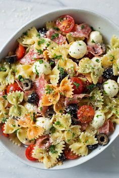 a white bowl filled with pasta salad on top of a marble countertop next to a fork