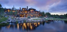 a large house sitting on top of a lush green hillside next to a lake at dusk