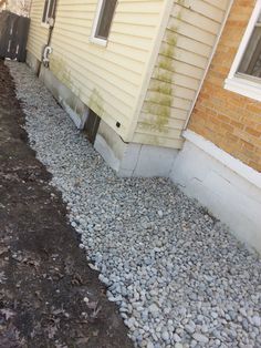 the side of a house with gravel and rocks on the ground next to it's door