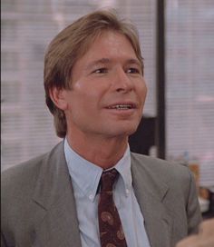 a man in a suit and tie talking to another man with his hand on his hip