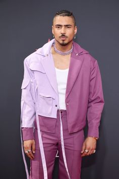 a man in a purple suit and white shirt standing on a red carpet with his hands in his pockets