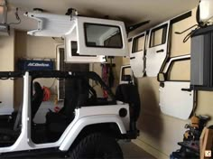 a white jeep parked inside of a garage next to a wall mounted mirror and door