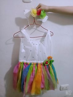 a child's dress hanging on a wall with a hand holding it up to the hanger