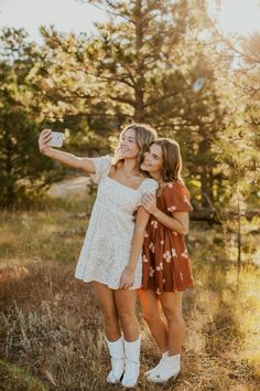 two young women taking a selfie with their cell phone in the woods at sunset