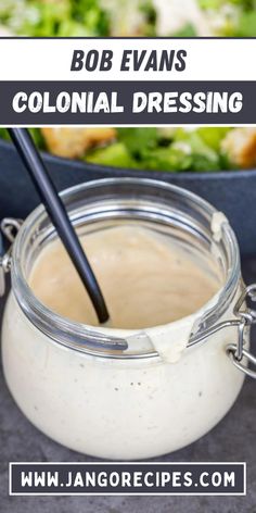 a jar filled with dressing sitting on top of a table next to a bowl of salad