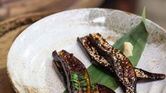 two pieces of food on a white plate with green leafy garnishes