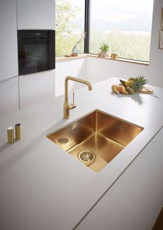 a white counter top with a gold sink and faucet next to it in front of a window