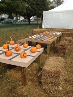 two tables with pumpkins on them in front of a tent and hay bales