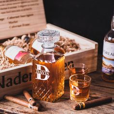 a bottle of whiskey and two glasses on a wooden table with cigars next to it