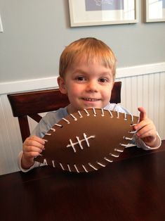 a young boy sitting at a table holding up a paper football