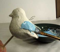 a white bird sitting on top of a blue plate with a paintbrush in it's beak