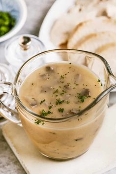 a glass pitcher filled with mushroom soup on top of a white plate next to bread