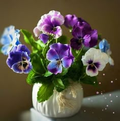 a white vase filled with purple and blue flowers