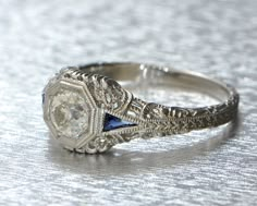 an antique diamond and blue sapphire ring on a white tablecloth with silver filigrees