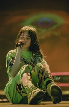 a woman sitting on the ground while holding a microphone in her hand and wearing green