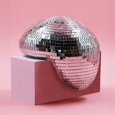 a shiny disco ball sitting on top of a pink block in front of a pink background