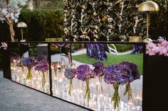 flowers and candles are arranged in vases on the side of a long glass table