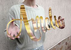 a woman holding up the word hello spelled in gold