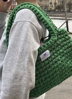 a woman walking down the street carrying a green handbag with a tag on it