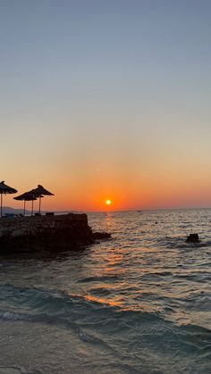 the sun is setting over the ocean with umbrellas in the foreground and people swimming in the water