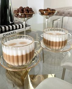 two desserts sitting on top of a glass table next to cups and saucers