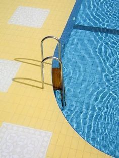 an empty swimming pool with yellow and blue tiles on the floor, next to a metal ladder