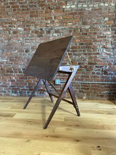 a wooden easel sitting on top of a hard wood floor next to a brick wall