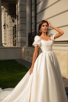 a woman in a white wedding dress standing on the sidewalk with her hand on her head