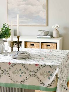 a dining room table covered with a white and green tablecloth next to a vase filled with flowers