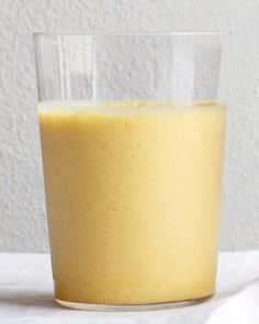 a glass filled with yellow liquid sitting on top of a white table next to a wall