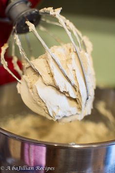 a whisk in a metal bowl with some white icing on it's side