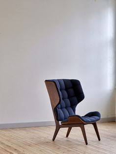 an upholstered chair sits in front of a white wall and wooden flooring