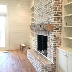 an empty living room with a brick fireplace and built - in shelving units on either side