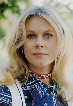 a woman with blonde hair wearing a blue and white dress standing in front of trees