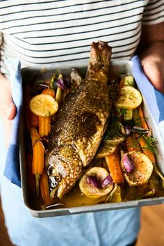 a person holding a tray with fish and vegetables