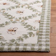 a white rug with green and brown flowers on it in the middle of a wooden floor