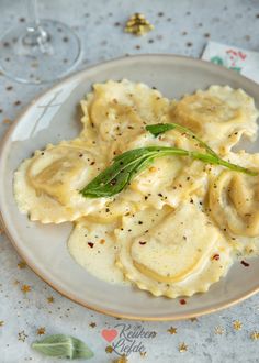 a white plate topped with ravioli covered in cheese sauce and garnished with herbs