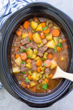 a crock pot filled with beef stew and carrots next to a blue towel